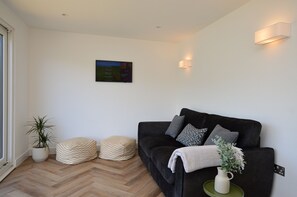 Una sala de estar moderna con un sofá negro, dos pufs, una planta en maceta y una obra de arte colgada en la pared.