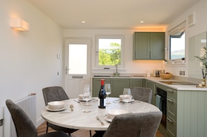 A dining area with a round table, chairs, and a bottle of wine.
