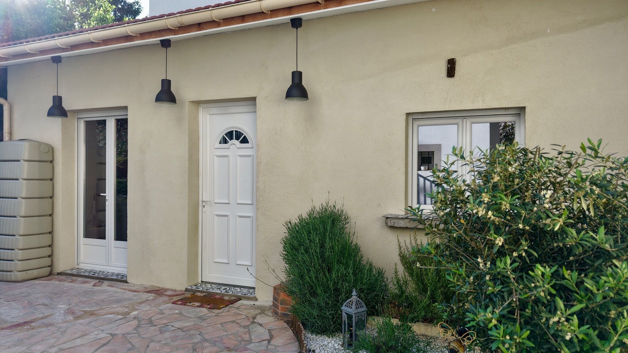 A building with a white door, a window with a view, and a small garden area with plants and a lantern.