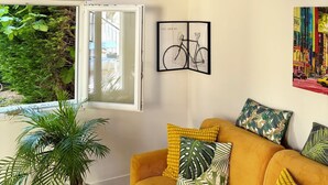 Ein Wohnzimmer mit Sofa, einem Blumentopf, Wandbildern und einem Fenster mit Blick.
