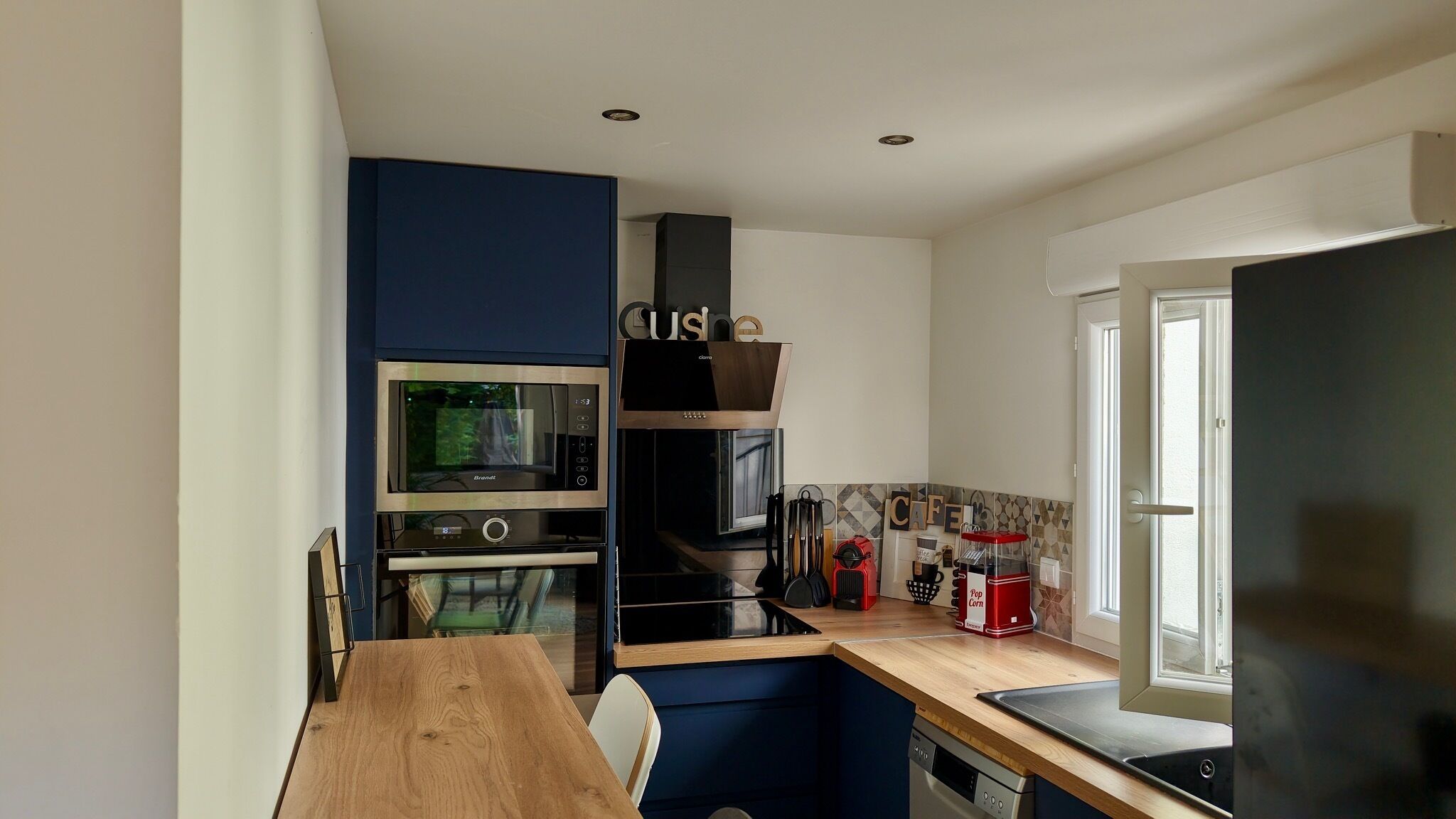 A compact kitchen with a wooden table, a built-in oven, a microwave, and a coffee machine.