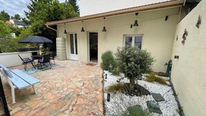 Eine Terrasse mit Steinboden, einem Tisch mit Stühlen, einer Bank und einem kleinen Baum.