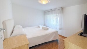 Una habitación de hotel con cama, televisión, ventana con cortinas y piso de baldosas.