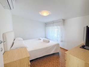 Ein Hotelzimmer mit Bett, Fernseher, Fenster mit Vorhängen und Fliesenboden.
