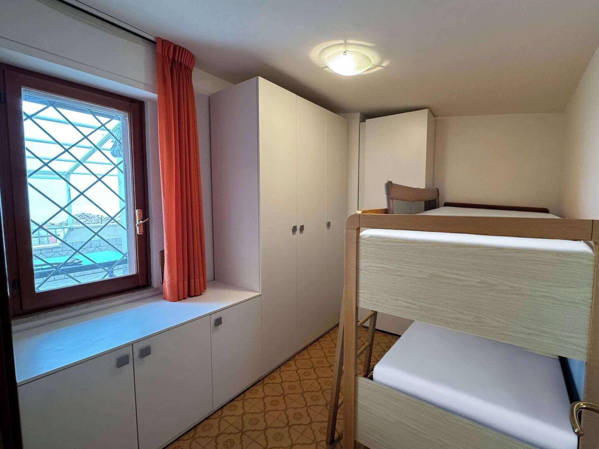 Una habitación con una cama litera, una ventana con cortina, un armario y una lámpara en el techo.