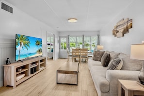 A modern living room with a TV, wooden console, sofa, and dining area. - Delphina in Anna Maria Island (Holmes Beach)