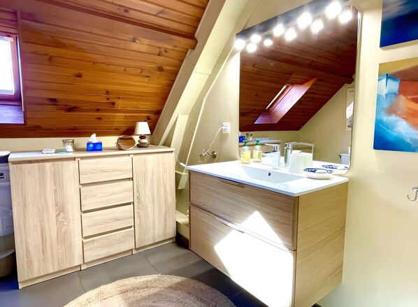 Un baño moderno con muebles de madera, un tocador con espejo y un tragaluz.