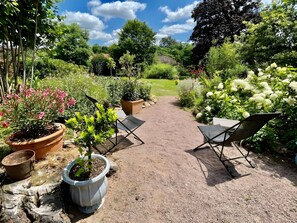 Un sendero en un jardín con plantas en macetas y dos sillas plegables.