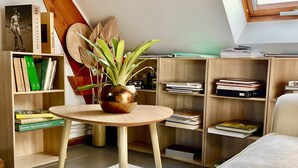 Una habitación con una mesa redonda de madera, una planta en maceta, estanterías y un sofá.