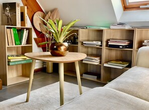 A room with a round wooden table, a potted plant, bookshelves, and a sofa.