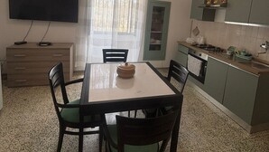 Une cuisine compacte comprenant une table à manger, des chaises, un téléviseur à écran plat et une fenêtre avec des rideaux.