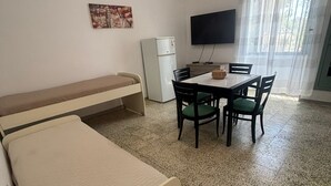 Une pièce comprenant un lit, une table avec des chaises, un téléviseur et un réfrigérateur.