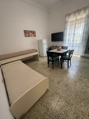 Ein Zimmer mit einem Bett, einem Tisch mit Stühlen, einem Fernseher und einem Kühlschrank.