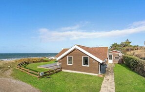 Ein Küstenhaus mit umzäuntem Garten, einem gepflasterten Weg und Blick auf das Meer.