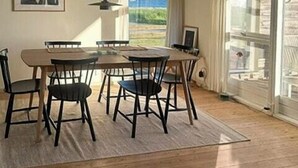 Ruokailutila, jossa on pöytä ja tuolit, riippuvalaisin ja näkymä lasiovesta.