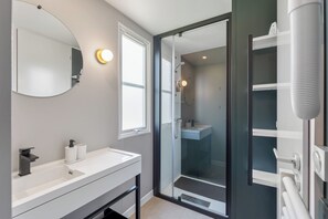 A modern bathroom with a white vanity, a large mirror, a glass shower enclosure, and a toilet. - Papillon (Bouillon)