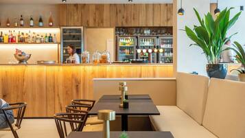 Een bar met houten lambrisering, een toonbank met flessen en zitplaatsen, inclusief een bank en stoelen.