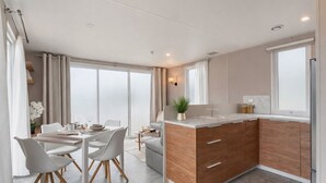 Una cocina moderna con una isla central, comedor con sillas y ventanas amplias.