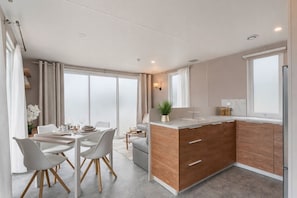 A modern kitchen with a central island, dining area with chairs, and large windows.