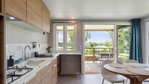 Una cocina moderna con estufa a gas, lavamanos y armarios de madera. Hay un comedor con mesa y sillas, y vistas a un balcón con mobiliario exterior.