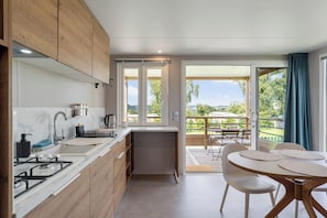 A modern kitchen with a gas stove, sink, and wooden cabinets. There is a dining area with a table and chairs, and a view of a balcony with outdoor furniture.