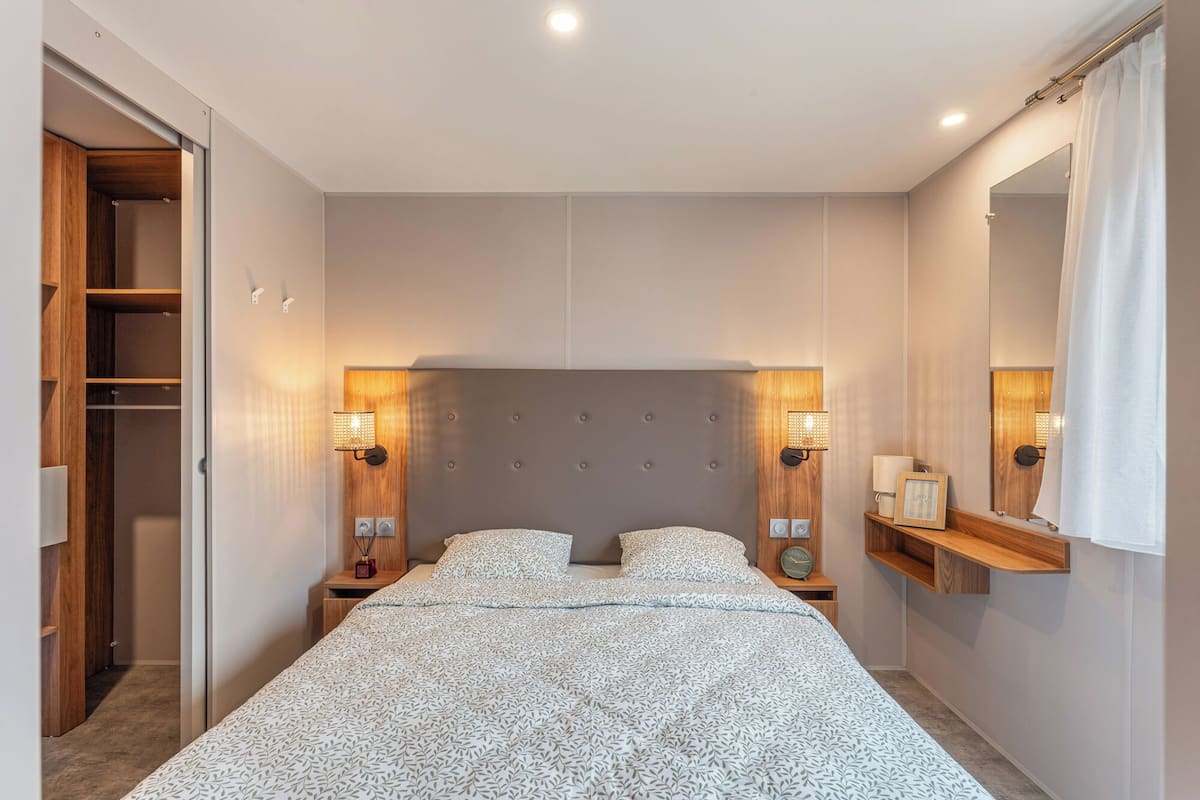 A bedroom with a large bed, two bedside tables, a wardrobe, and a mirror.