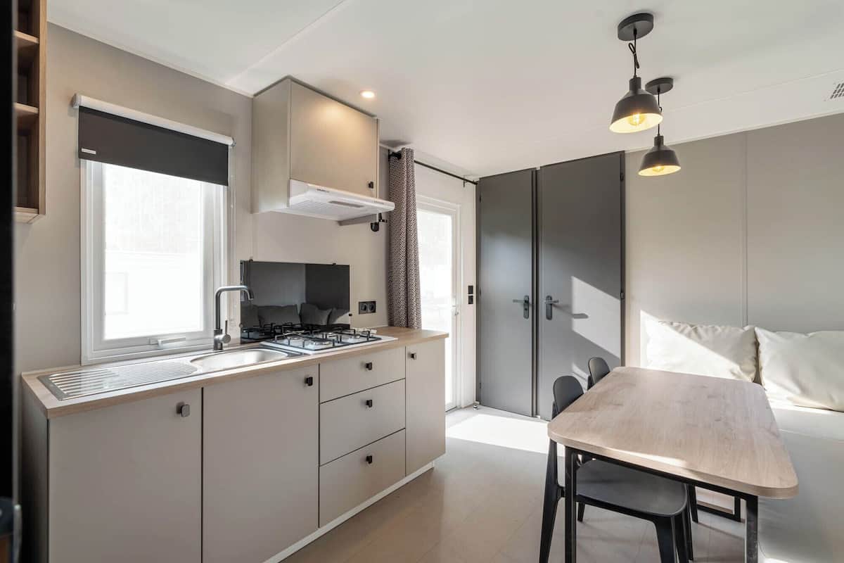 A modern kitchen with a gas stove, a built-in oven, and a window. There is a dining area with a table and chairs.