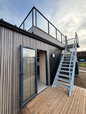 A modern building with a wooden exterior, a large sliding glass door, and a metal staircase leading to an upper level. - Papillon (Bouillon)