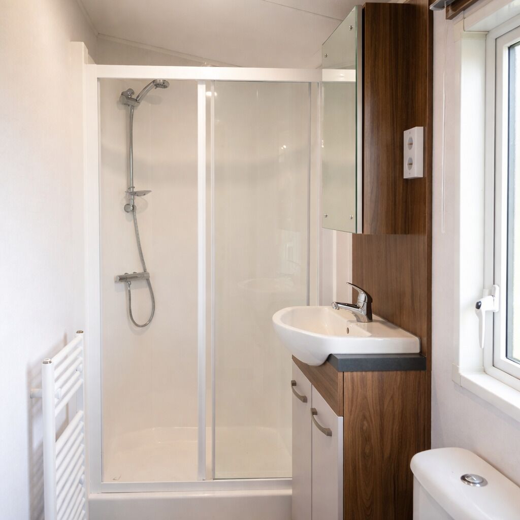 A modern bathroom with a glass-enclosed shower, a white sink, and a wooden vanity.