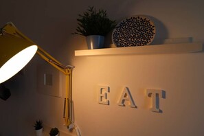 Un mur sur lequel est écrit le mot « MANGER » en grandes lettres, une plante en pot et une assiette décorative posée sur une étagère.