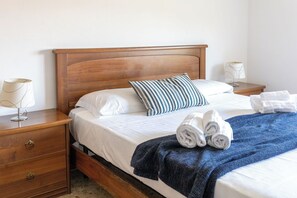 Ein ordentlich bezogenes Bett mit weißen Leinen, einem gestreiften Kopfkissen und aufgerollten Handtüchern auf einem Holz-Kopfteil.