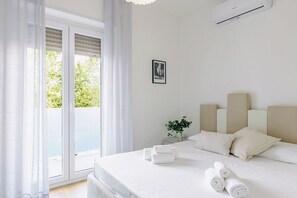 Ein Hotelzimmer mit Bett, Nachttisch, Topfpflanze und einem Fenster mit Vorhängen.