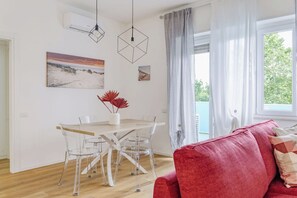 Ein modernes Wohnzimmer mit Essbereich, transparenten Glasstühlen, einem Holztisch und einem roten Sofa.