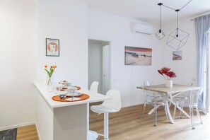 Een moderne eethoek met een witte tafel, transparante stoelen en een hanglamp.