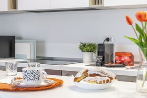 Una cucina moderna con una macchina da caffè, una pianta in vaso, una tazza di caffè, un pasticcino e una confezione di cialde per caffè.