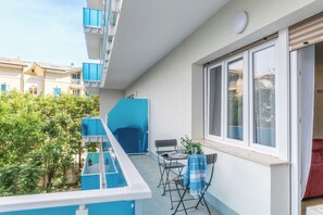 Un balcone con tavolo e sedie, una pianta in vaso e vista sugli edifici vicini.