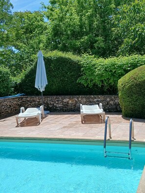 A pool area with two lounge chairs and a sun umbrella.