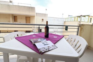 Une table de balcon avec une bouteille de vin, deux verres et un magazine.