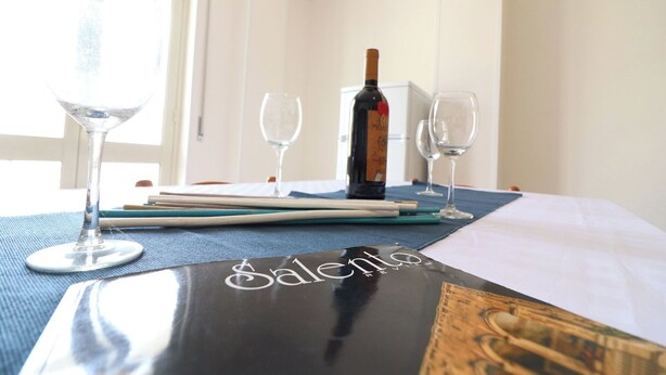 A hotel room with a bed, a table with wine glasses and a bottle, and a menu on the table. - Wonderful  villa for 4 guests with A/C, WIFI, TV and balcony (Otranto)