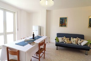 Un coin repas avec une table dressée pour deux personnes, un canapé et un réfrigérateur en arrière-plan.