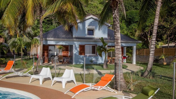 A house with a pool, surrounded by palm trees and outdoor seating. - Fully Furnished 3-Bedroom Apartment (Saint-Leu)
