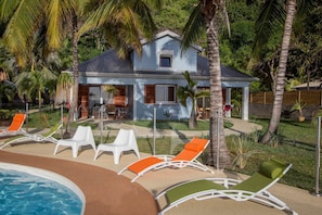 A house with a pool, surrounded by palm trees and outdoor seating. - Fully Furnished 3-Bedroom Apartment (Saint-Leu)