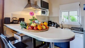 A kitchen with a central island, a microwave, a coffee maker, and a window with a view of greenery. - Fully Furnished 3-Bedroom Apartment (Saint-Leu)