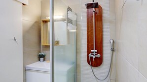 A bathroom with a glass shower enclosure, a wooden showerhead, and a white sink with a small potted plant. - Fully Furnished 3-Bedroom Apartment (Saint-Leu)