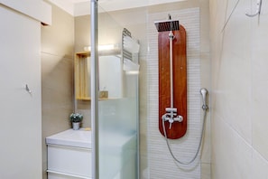 A bathroom with a glass shower enclosure, a wooden showerhead, and a white sink with a small potted plant.