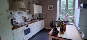 A kitchen with white cabinets, a wooden countertop, a sink, a kettle, and a dining table with chairs.