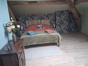 A bedroom with a wooden ceiling, floral wallpaper, a bed with a green bedspread, and a vase with flowers. - Bed and Breakfast 'La Chambre Des Papillons' with Shared Pool, Private Terrace and Wi-Fi (Moissannes)