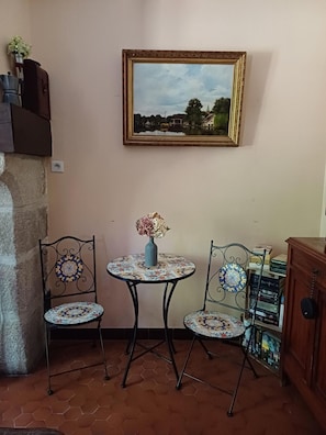 Un pequeño comedor con dos sillas, una mesa, un jarrón con flores, un cuadro en la pared y una estantería llena de libros.