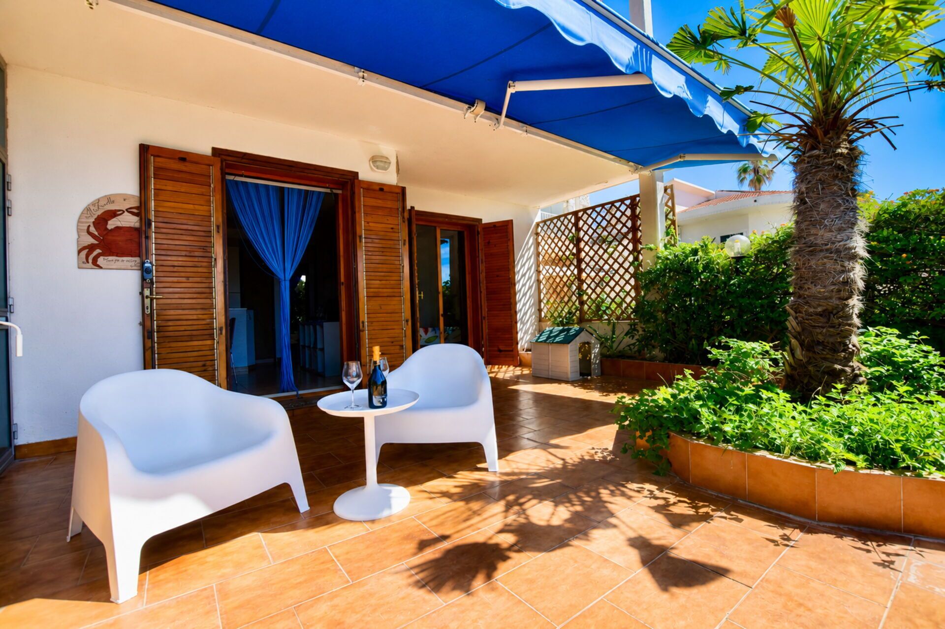 A patio with two white chairs, a small round table, and a bottle of wine.