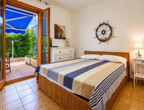 Ein Schlafzimmer mit einem Bett, einem Nachttisch, einem fest montierten Schiffsschwungrad, einem Gemälde und einer Glastür, die zu einem Außenbereich führt.
